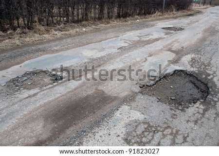 Damaged asphalt pavement road with potholes caused by freeze and thaw cycle during winter.
