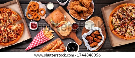 Table scene of assorted take out or delivery foods. Hamburgers, pizza, fried chicken and sides. Top down view on a dark wood banner background. Stockfoto © 