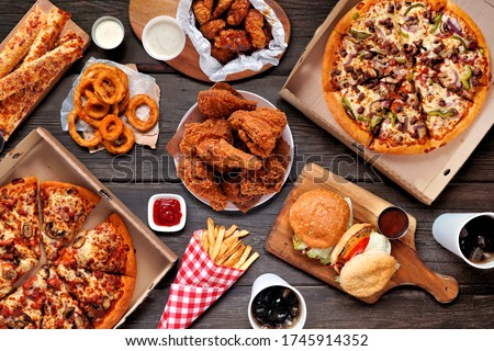 Buffet table scene of take out or delivery foods. Pizza, hamburgers, fried chicken and sides. Above view on a dark wood background. Stockfoto © 