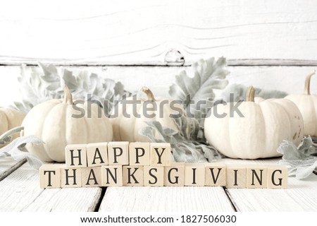 Photo of Happy Thanksgiving greeting on wooden blocks against a white wood background with white pumpkins and autumn leaves