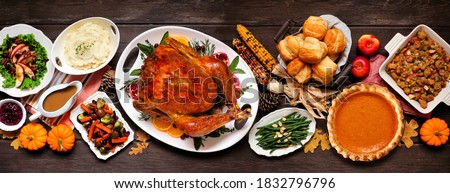Traditional Thanksgiving turkey dinner. Top view table scene on a dark wood banner background. Turkey, mashed potatoes, dressing, pumpkin pie and sides.