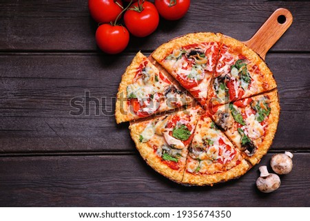Healthy, gluten free cauliflower crust pizza with tomatoes, mushrooms and spinach. Top down view with cut slices. Table scene on a dark wood background.