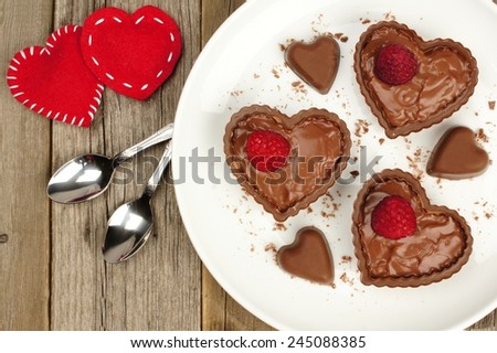 Heart shaped chocolate dessert cups with pudding and raspberries on plate with wood background