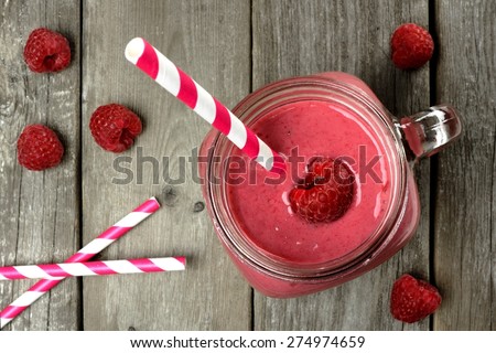 Pink raspberry smoothie in a mason jar with straws, overhead view on rustic wood background