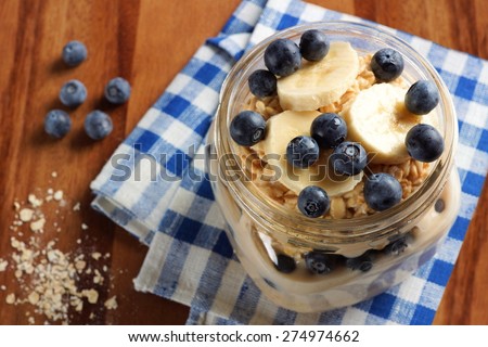 Blueberry and banana breakfast overnight oatmeal in a mason jar, with checkered cloth on wood