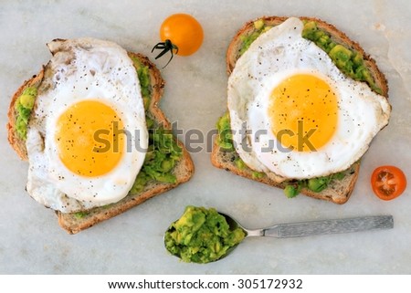 Open avocado, egg sandwiches on whole grain bread against a marble background