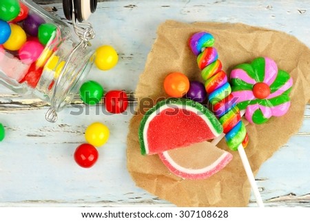 Sweet candies in a cluster on paper with rustic wood background and spilling candy jar