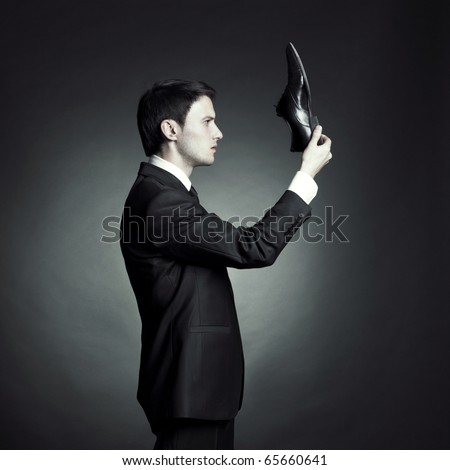 Surreal portrait of a stylish man in an elegant suit and shoes in hand