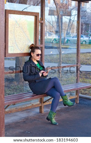 Girl sitting on a bench waiting for transport at the bus stop. Waiting for transport studies mobile phone