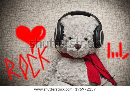 Toy teddy bear with a red scarf listening to music on headphones. Fan of Rock music