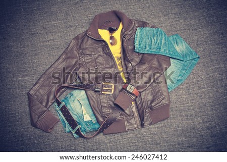 City youth fashion clothing. Brown jacket, blue jeans, T-shirt, belt, watches and sunglasses. Photo toned in vintage style