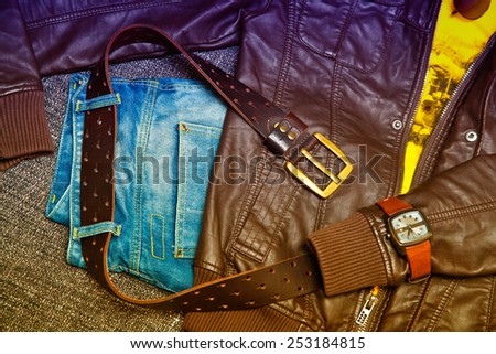 Fashion trend: leather jacket, blue jeans, a belt with a gold buckle, watch. Photo toned in yellow and purple