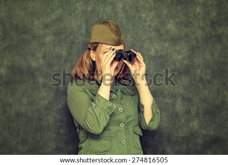 Girl in garrison cap during the Second World War, looking through binoculars. Vintage style. Victory Day on May 9.