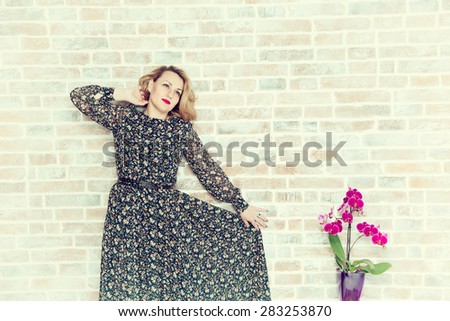 woman in a beautiful dress in the movement and home flower in pot. Against the background of a brick wall