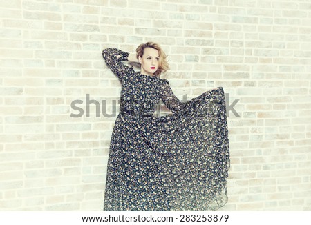 Beautiful woman lifted the hem of her dress and posing against a brick wall background