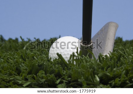 golf ball on tee on grass with blue sky and golf club