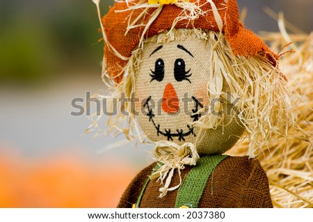 Autumn, fall decoration at pumpkin patch featuring a scarecrow and wagon with straw and pumpkins in the background
