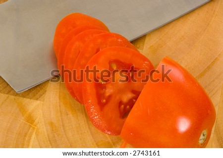 Sliced roma tomato with edge of knife on wooden cutting board