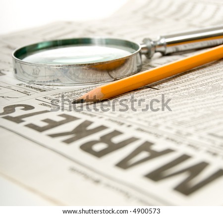 Newspaper open to market section wit tools for research, pencil and magnifying glass