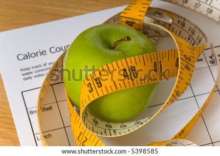 Items that would be associated with dieting or losing weight, including a tape measure, an apple, and a calorie counting chart, focus on top of apple, calorie chart is blurry