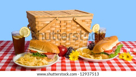 A picnic lunch consisting of a sandwich, potato chips and grapes on a red gingham tablecloth with iced tea and a lemon