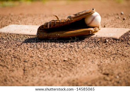 A brown leather baseball glove and a white leather baseball on a pitcher\'s mound at a baseball field, with copy space