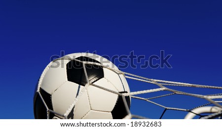 A traditional soccer ball or football in a goal net in front of a blue sky