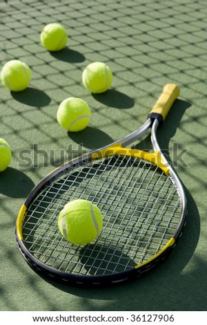 A group of tennis balls and a tennis racket on a freshly painted cement tennis court