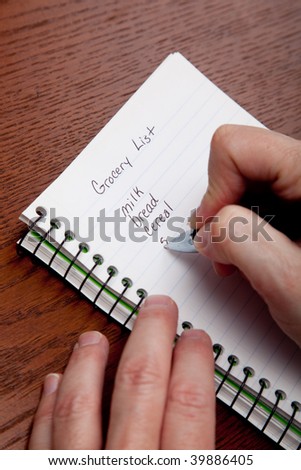 Hands writing a shopping list with a wooden desk background