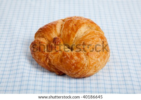 A single croissant on a blue gingham table cloth