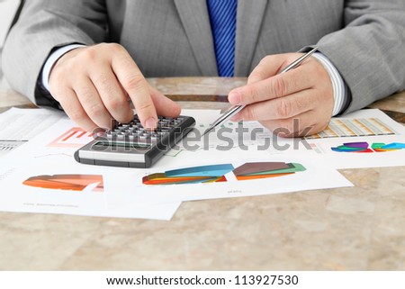 Male Hand with Pen Using Calculator on the Table with Charts