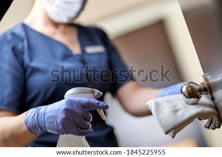 Maid in mask doing disinfecting the door handle in hotel