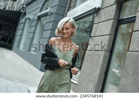 Foto Bild Stilvolle blonde Frau, die im Regen spazieren geht. Sie hält einen schwarzen Regenschirm in einem nicht gesperrten Bereich.