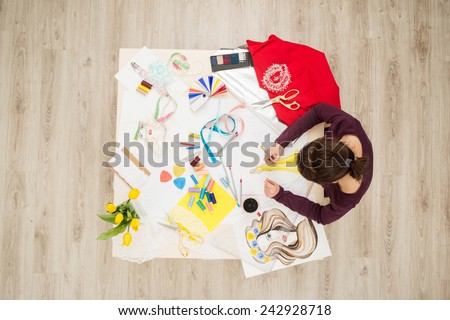 Top view of table full of creative things with young woman drawing. Fashion designer concept
