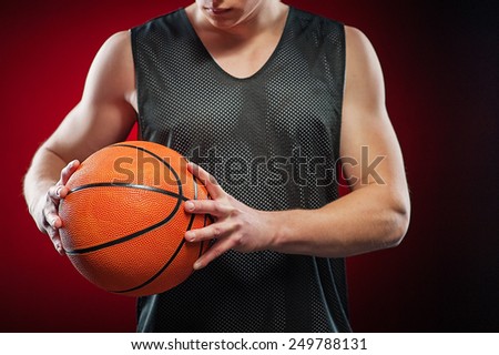Young male basketball athlete gripping with two hands the ball tightly on red background
