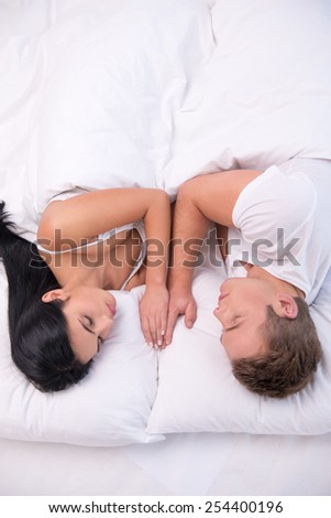 Top view photo of sleeping young couple lying in white bed under white blanket