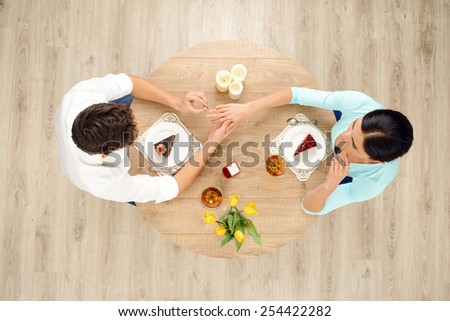 Top view of round table with couple on date. Man putting ring on the right hand of woman. Proposal of marriage concept
