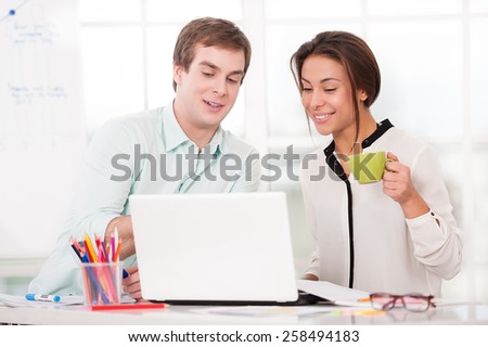 Young creative businessman and mixed race businesswoman working with laptop. Office interior with window