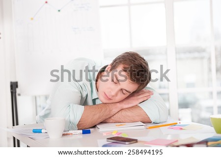 Young tired businessman sleeping while working day. Office interior with window