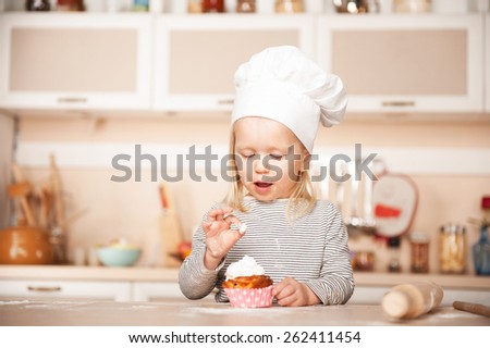 Little cute girl with chef hat tasting cake. Kitchen interior. Concept for young kitchen hands