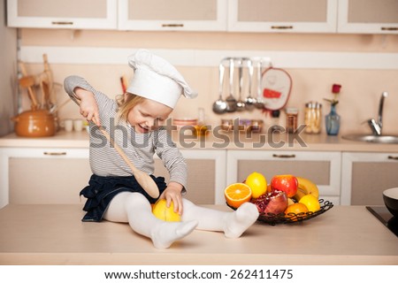 Little cute girl with chef hat holding big wooden spoon while cooking. Kitchen interior. Concept for young kitchen hands