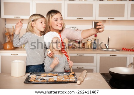 Little cute girls and their mother making photo while preparing cookies. Kitchen interior. Concept for young kitchen hands