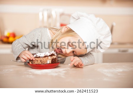 Little cute girl with chef hat eating cake. Kitchen interior. Concept for young kitchen hands
