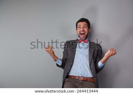 Portrait of positive casual young man wearing tweed jacket and red bow tie. Man showing his happiness and success
