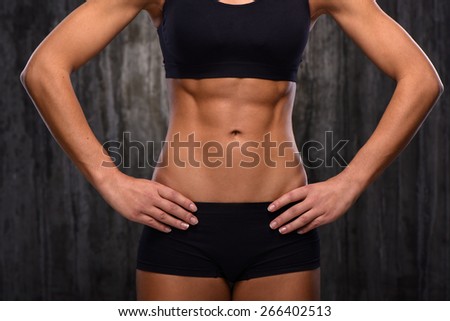 Close up photo of young mixed race sporty woman. She demonstrating her biceps and slim belly. Fitness concept