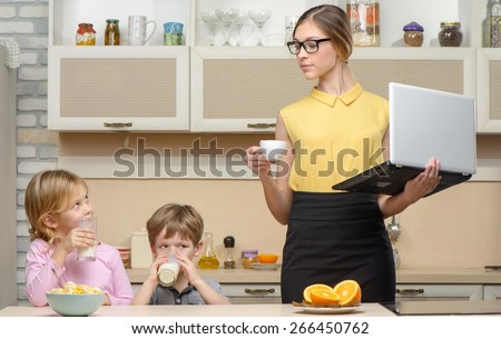 Young business woman early in the morning with her little children. She using laptop. Kitchen interior. Concept for busy mother