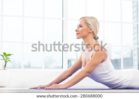 Close up photo of beautiful woman practicing yoga. Woman meditating while doing cobra pose. White interior with large window