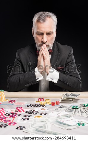Man in years sitting at poker table and considering poker strategy. The chips and money are on table