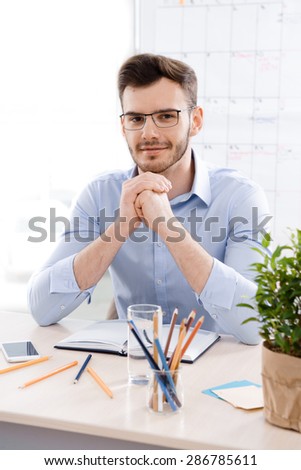 Young businessman wearing glasses is in office full of folders for documents and office supplies. Businessman looking at the camera