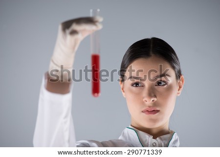 Close up photo of woman wearing protective clothing and gloves. Woman holding test tube and looking at it